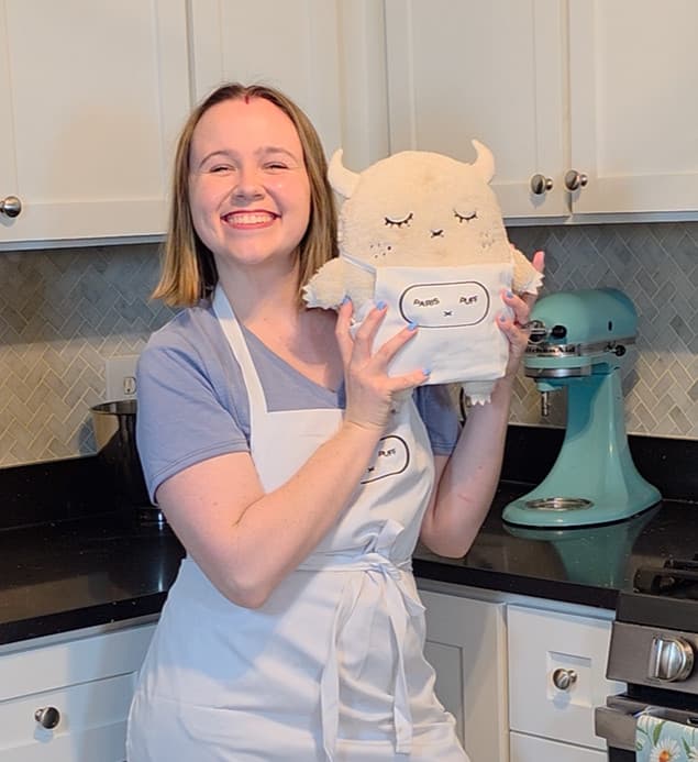 Paris holding Puff in the kitchen, wearing matching Paris x Puff aprons